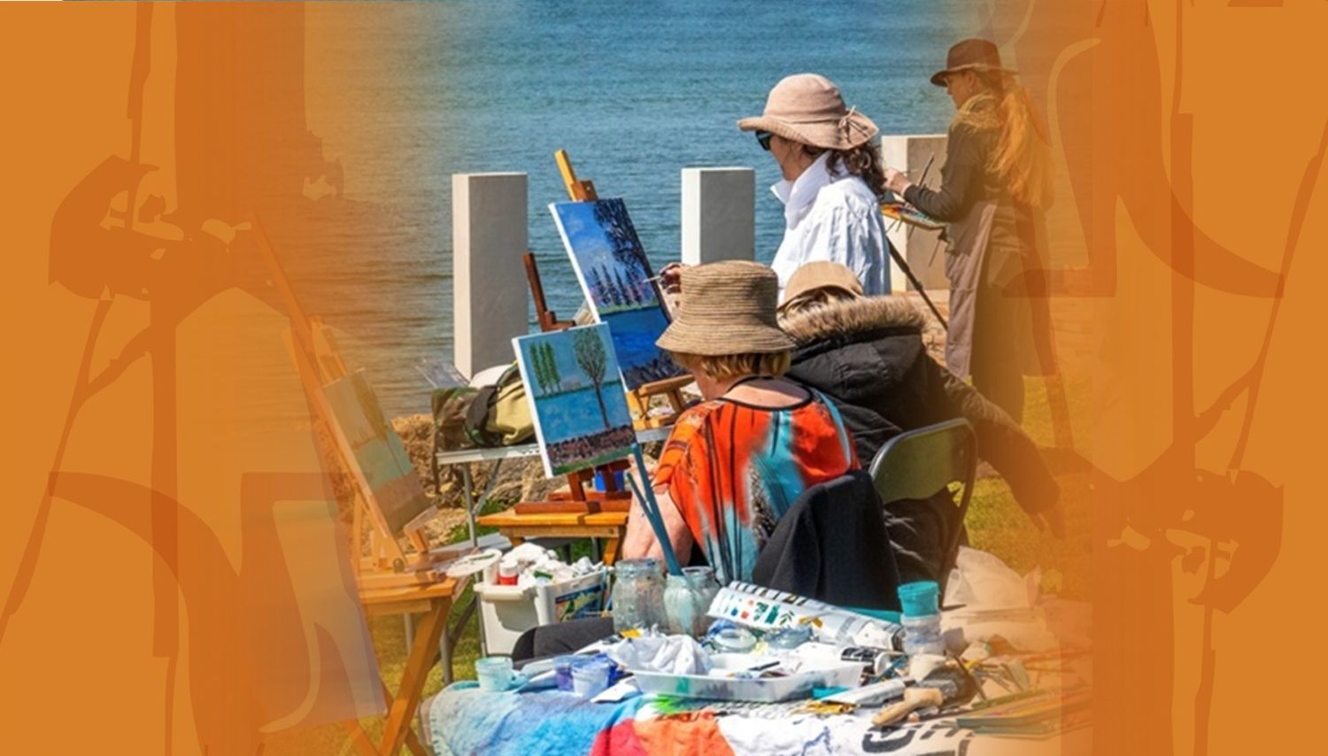 A group of people sit along the water's edge with mini easels, painting the landscape before them